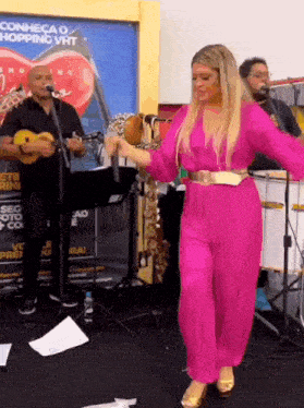 a woman in a pink jumpsuit is dancing in front of a man playing a guitar