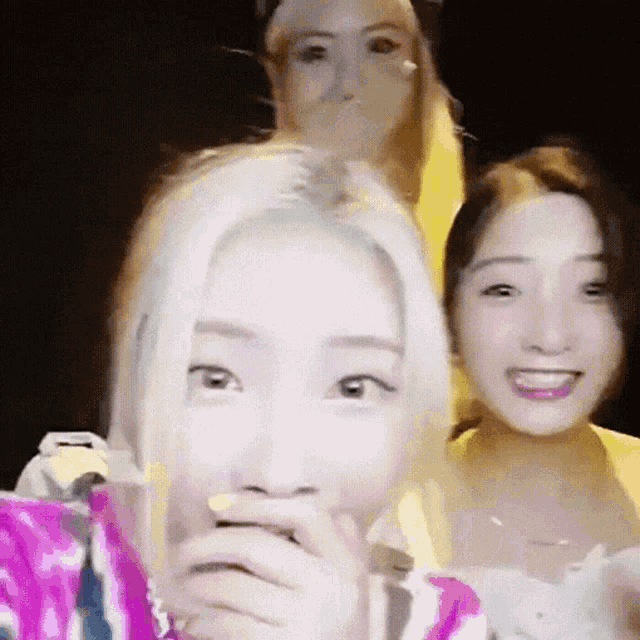 a group of three women are standing next to each other and one of them is covering her mouth with her hand