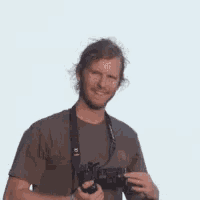 a man in a brown shirt is holding a canon camera