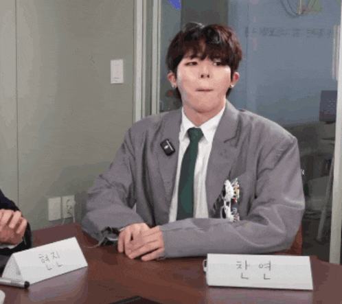 a man in a suit and tie sits at a table with a name tag that says l on it
