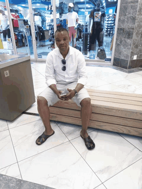 a man sits on a wooden bench in front of a store that says ' o'neill ' on the front of it
