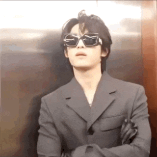 a man wearing sunglasses and a suit is standing in an elevator .