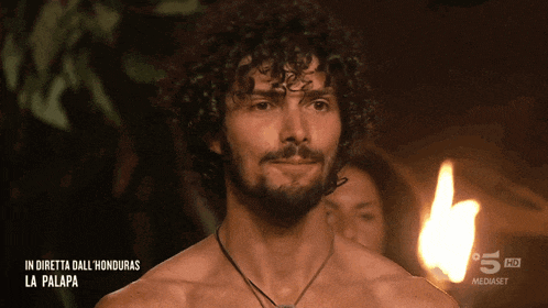 a man with curly hair and a beard is standing in front of a fire with the words in diretta dall honduras la palapa