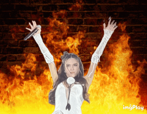 a woman in a white dress is holding a microphone in front of a fire background