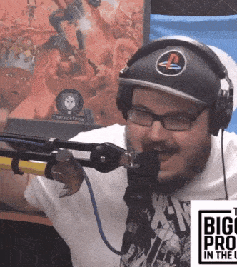 a man wearing headphones and a hat with a playstation logo stands in front of a microphone