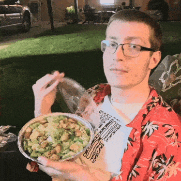 a man wearing a hawaiian shirt is eating a salad outside