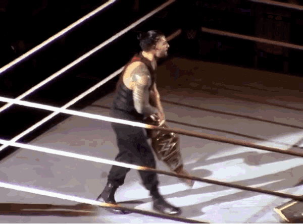 a wrestler in a black tank top and black pants is standing in the middle of a wrestling ring