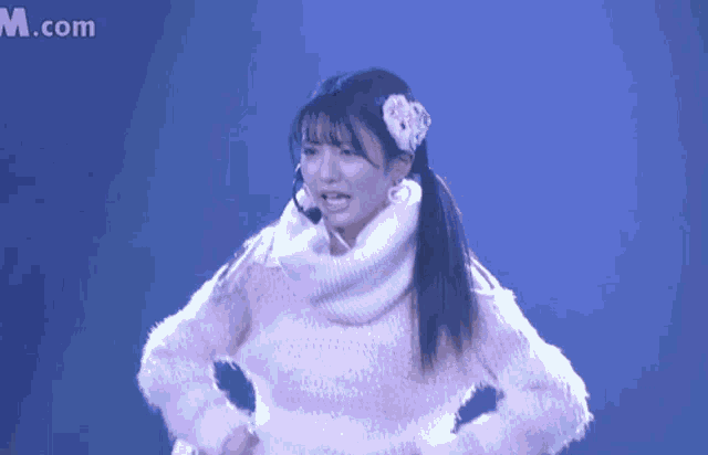 a girl wearing a pink sweater and a white scarf stands in front of a m.com logo