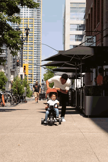 a man pushes a child in a stroller on a sidewalk in front of a whip hand restaurant