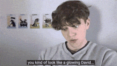 a young man says you kind of look like a glowing david in front of a wall with cartoons on it .