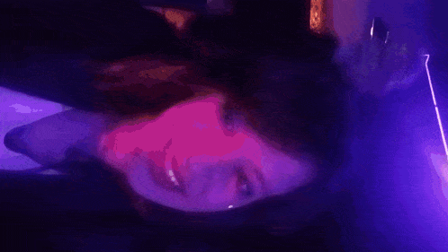 a woman 's face is lit up with purple lights in a dark room