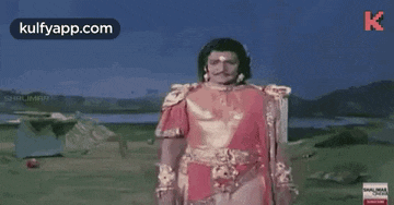 a man in a red and gold costume is standing in a field in front of a lake .