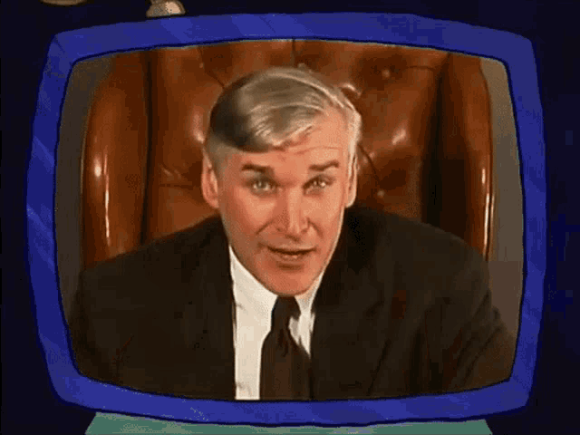 a man in a suit and tie is sitting in front of a television screen .