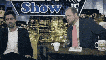 two men are sitting in front of a show sign