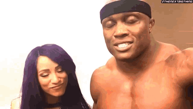 a man and a woman are standing next to each other . the woman has purple hair and the man is shirtless .