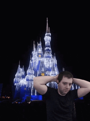 a man holds his hands behind his head in front of a disney castle