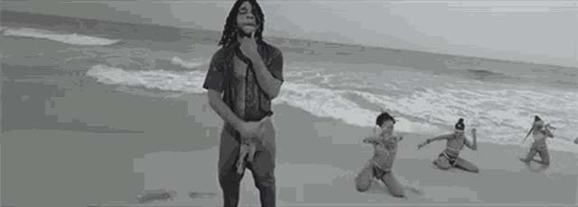 a black and white photo of a man standing on a beach next to a group of women .