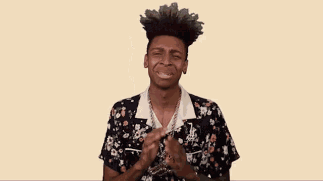 a young man wearing a floral shirt and a chain is clapping his hands .