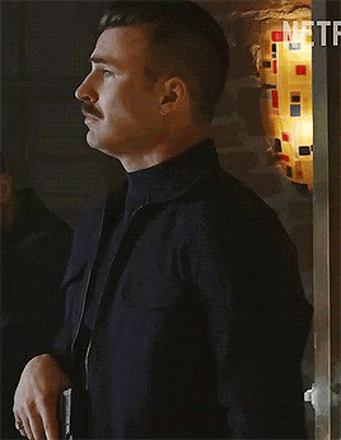 a man with a mustache is standing in front of a wall with netflix written on it