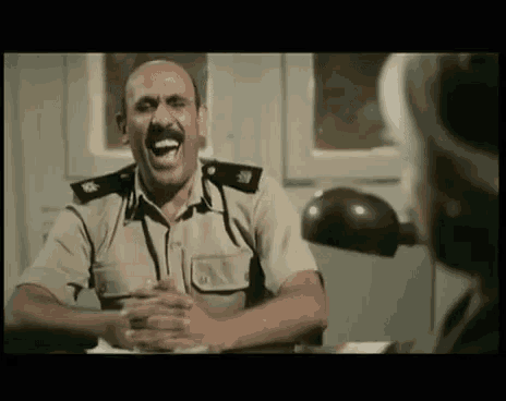 a man in a military uniform is laughing while sitting at a table .