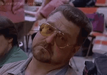 a man with a beard wearing sunglasses is sitting in a crowded room .