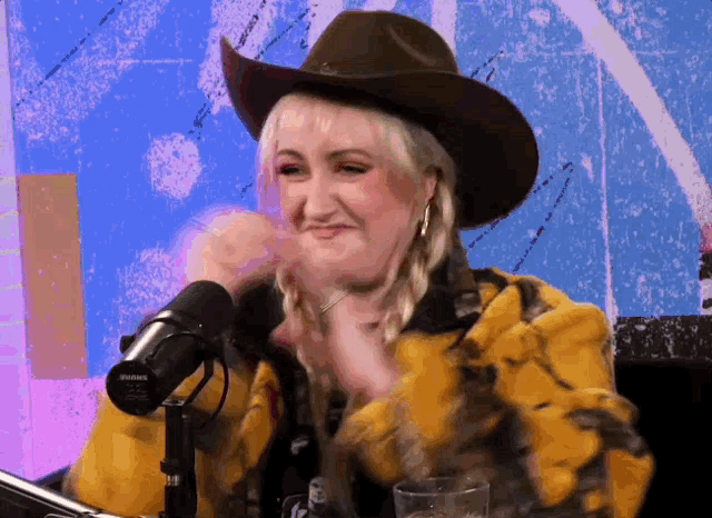 a woman wearing a cowboy hat is sitting in front of a microphone