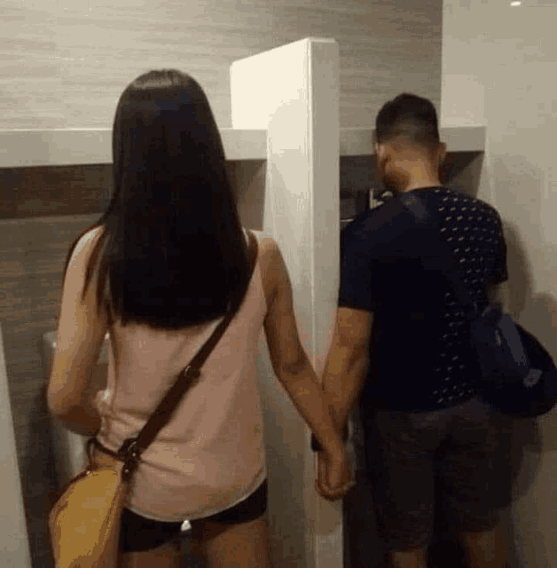 a man and a woman are holding hands in a public bathroom .