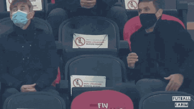 a man wearing a face mask sits in a stadium with a fly emirates seat cover