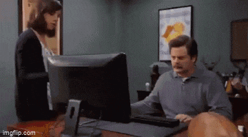 a man is sitting at a desk using a computer while a woman stands behind him .