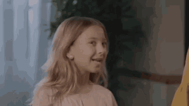 a little girl wearing a pink shirt and earrings is smiling .