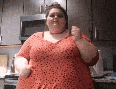a woman in a red polka dot shirt is standing in a kitchen