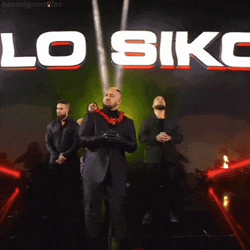 a group of men are standing in front of a large sign that says lo siko