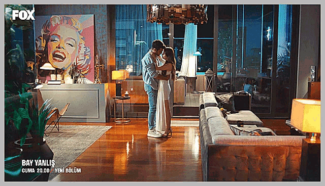 a man and woman are hugging in a living room with a fox logo on the corner