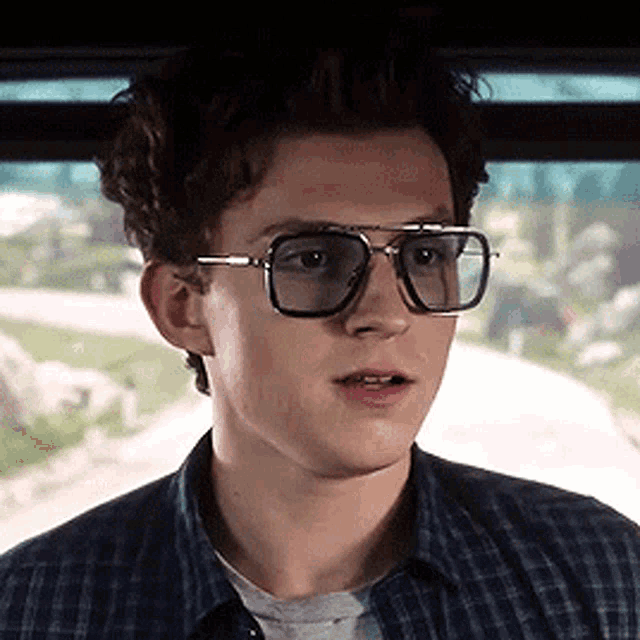 a young man wearing glasses and a plaid shirt is looking out a window .