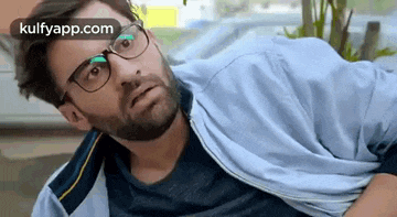a man with glasses and a beard is wearing a blue jacket and a blue shirt .