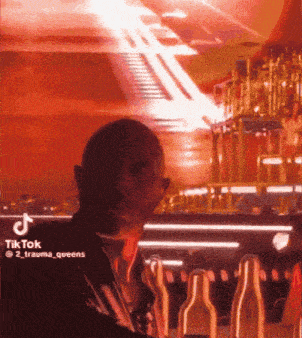 a man is standing in front of a bar with bottles and a tik tok sticker