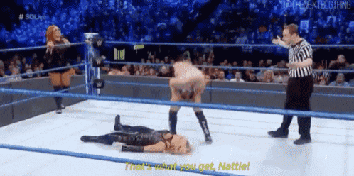 a wrestler is laying on the floor in a wrestling ring while a referee watches .