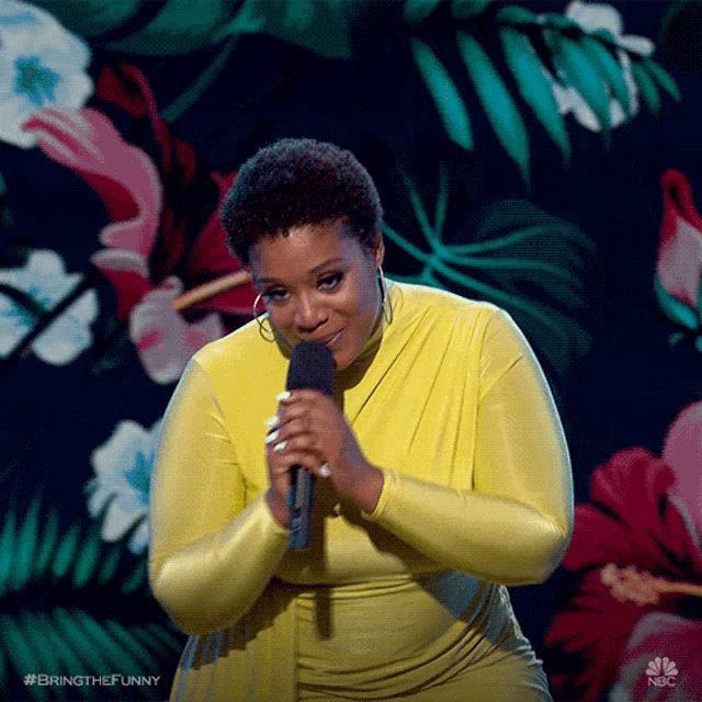 a woman in a yellow dress is holding a microphone in front of a floral background .