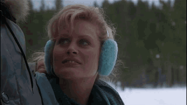 a woman wearing furry ear warmers is standing in the snow .
