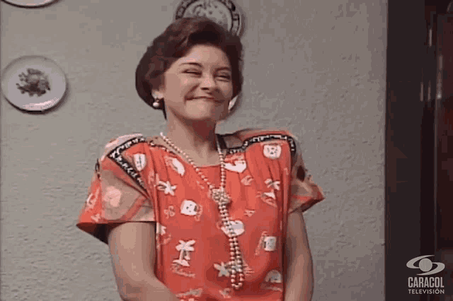 a woman wearing a red shirt and a pearl necklace is smiling for a photo taken by caracol television