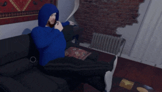 a man in a blue hoodie sits on a black couch