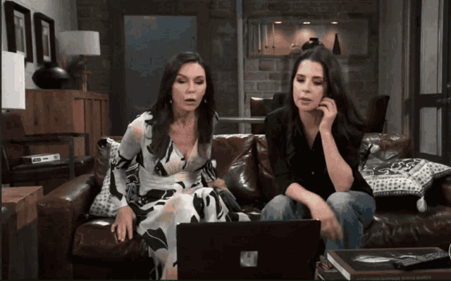 two women sitting on a couch looking at a laptop that says microsoft