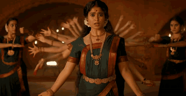 a woman in a green and red dress stands in front of a group of female dancers
