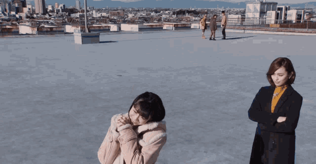 a group of people standing on a rooftop with a city in the background including a woman in a pink coat