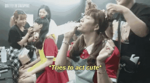 a group of girls are sitting in a room and one of them is drinking from a bottle and says `` tries to act cute ''