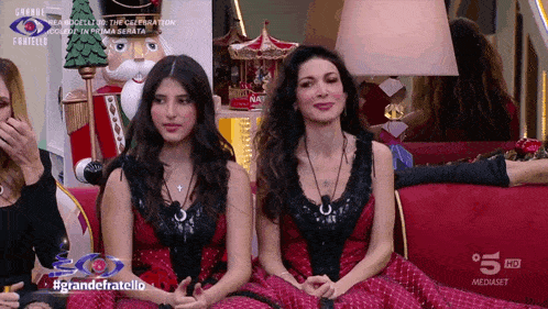 two women are sitting on a red couch in front of a nutcracker on a television screen