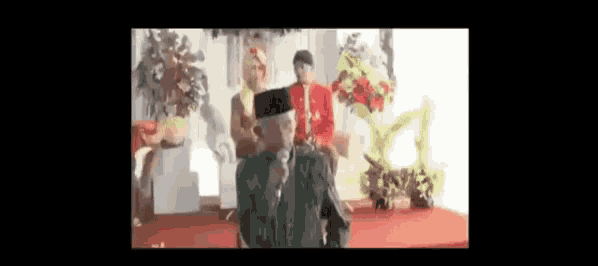 a man is standing in front of a microphone in a room with a bride and groom .