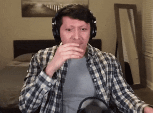a man wearing headphones and a plaid shirt is covering his mouth