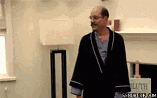 a man in a robe is standing in a living room next to a lamp .