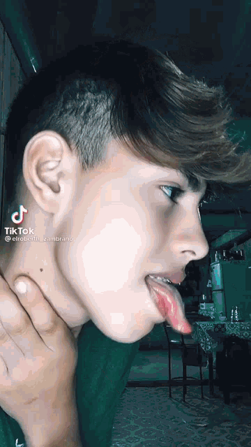 a young man is sticking his tongue out while wearing a green shirt .
